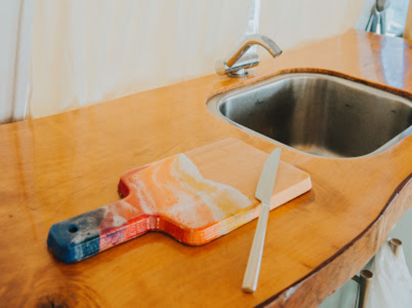 Compact RV rental kitchen with a beautiful wooden counter, sink, and a colorful cutting board with a knife. Ideal for travel.