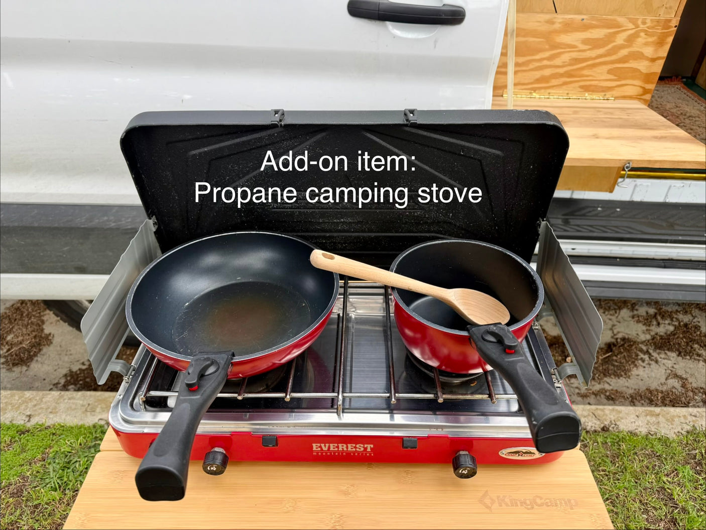 RV rental add-on: Red propane camping stove with pan and pot on a wooden table, ready for outdoor cooking.