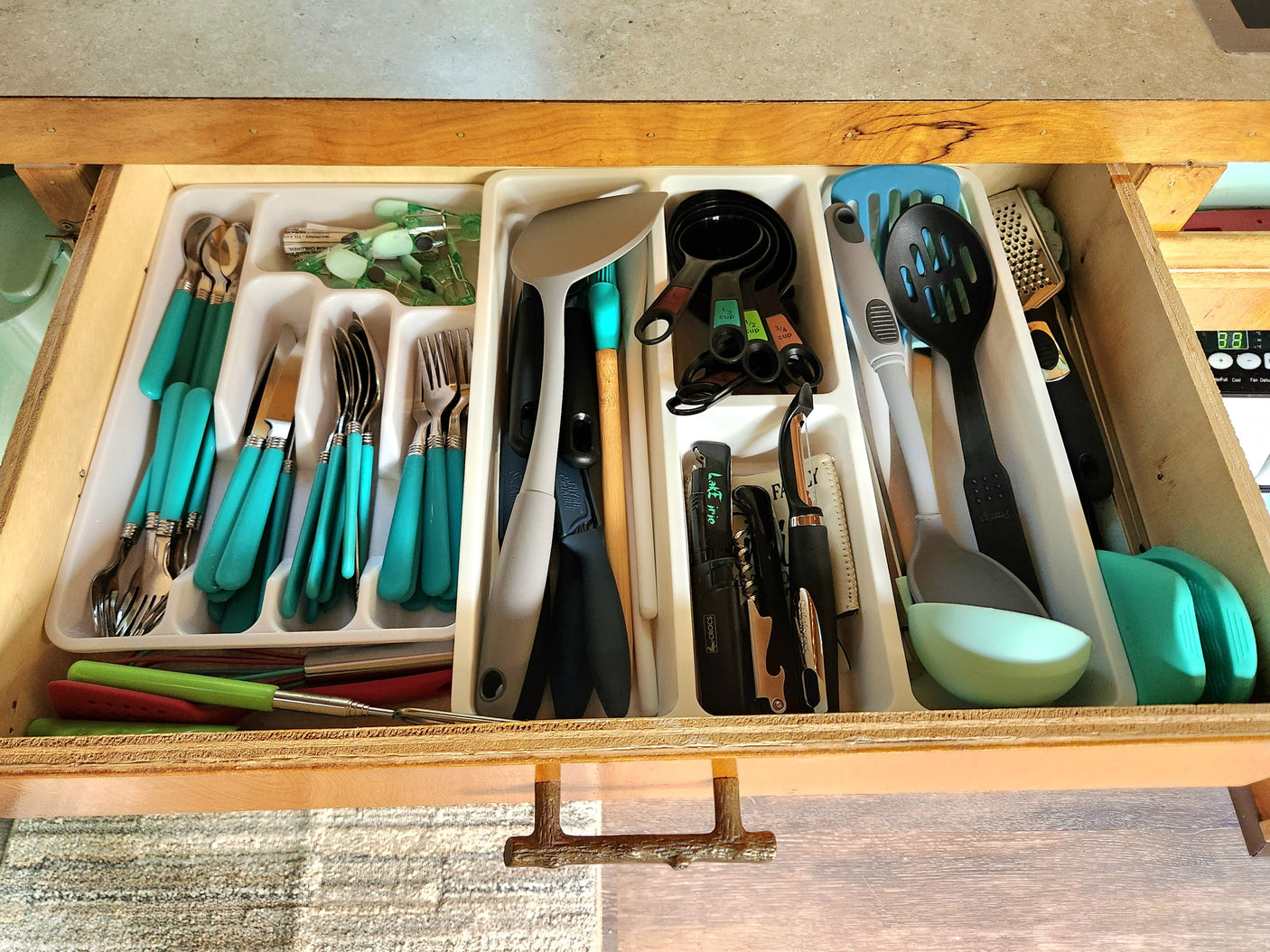 RV rental kitchen drawer shows organized teal cutlery, measuring cups, and various cooking utensils for easy access.