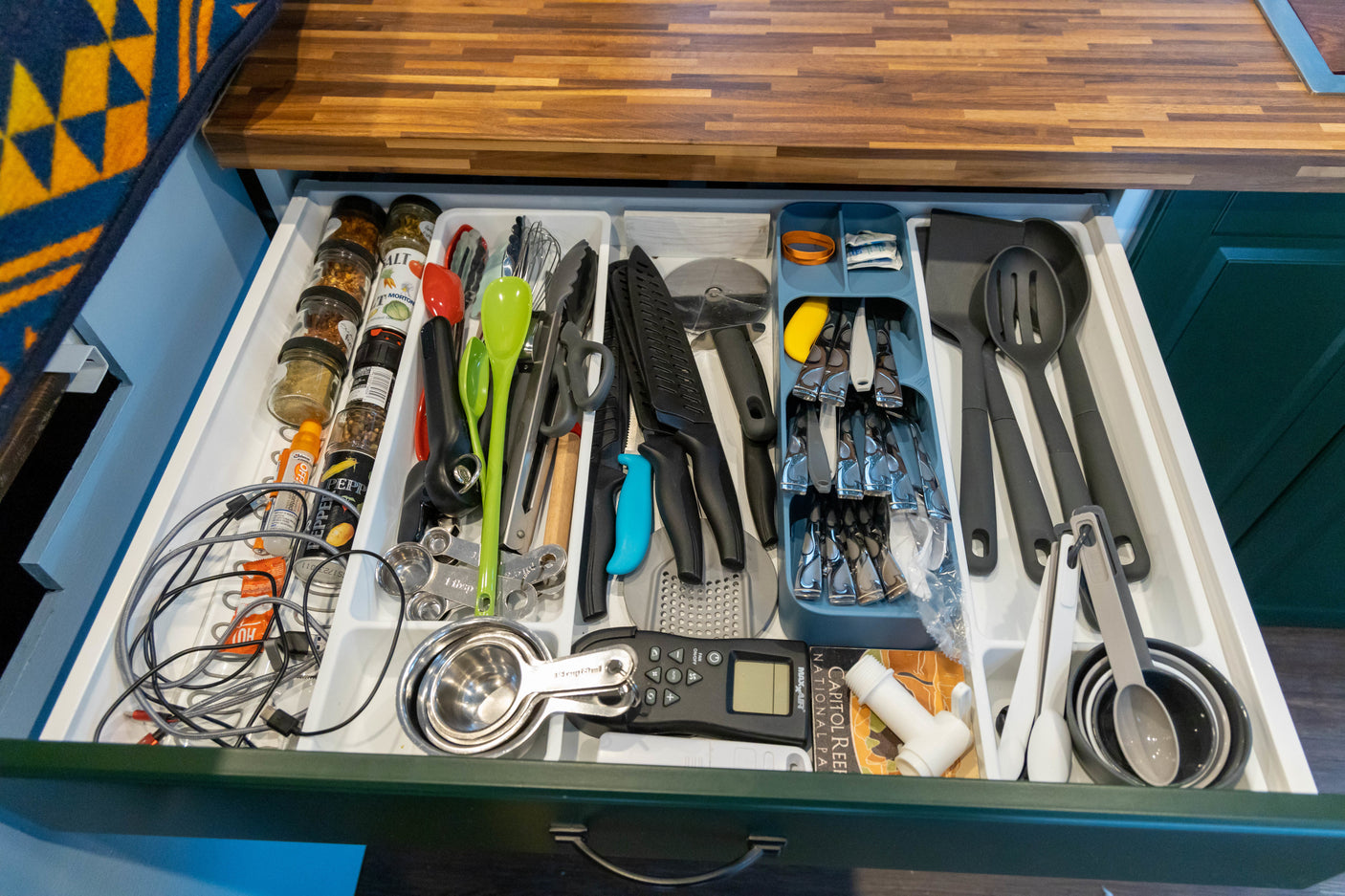 Neatly organized RV rental kitchen drawer featuring cooking utensils, spices, measuring cups, and flatware, optimized for compact living.