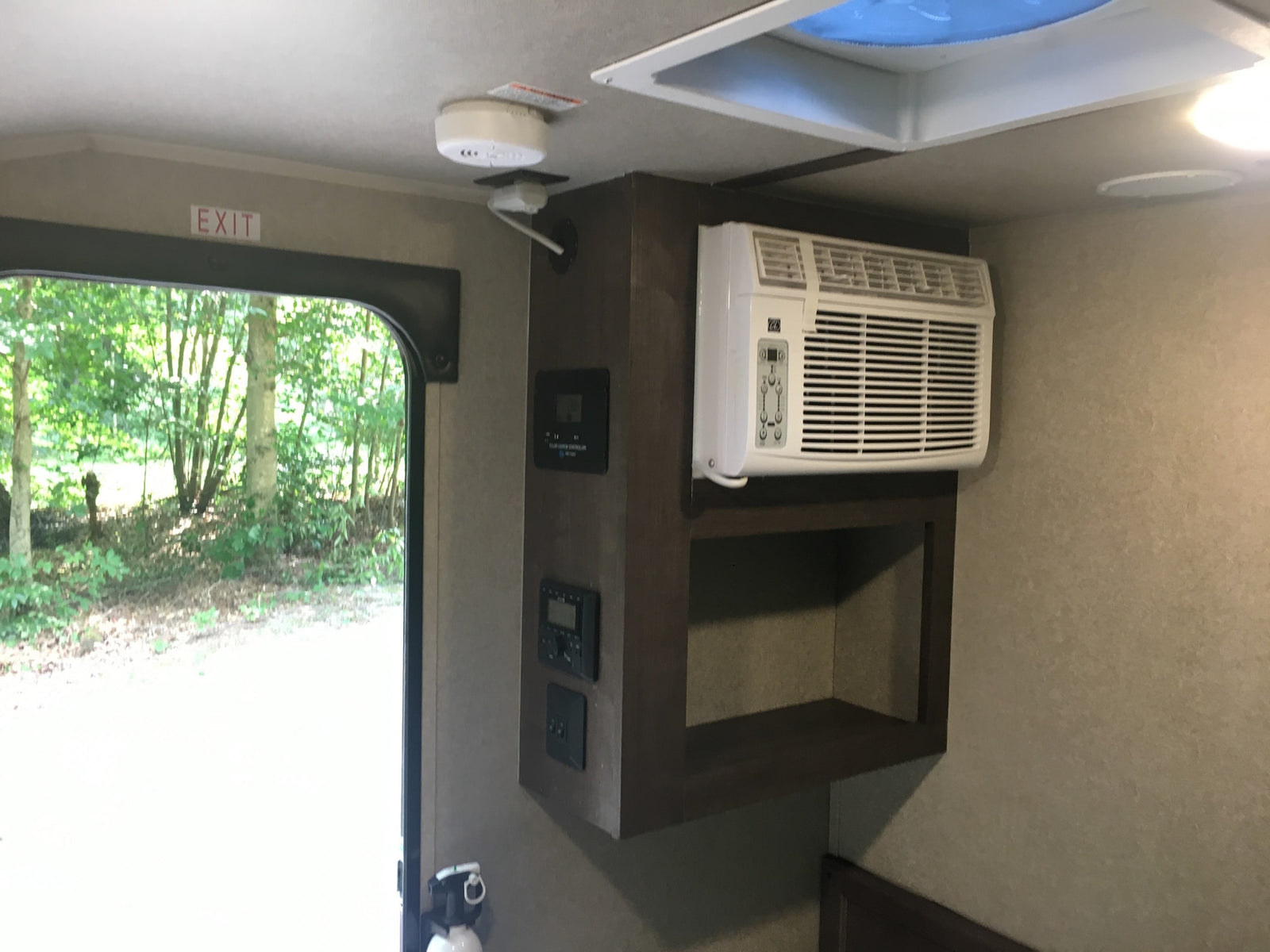 RV rental interior: AC unit, control panel, exit door to nature. Includes smoke alarm & fire extinguisher for safety.