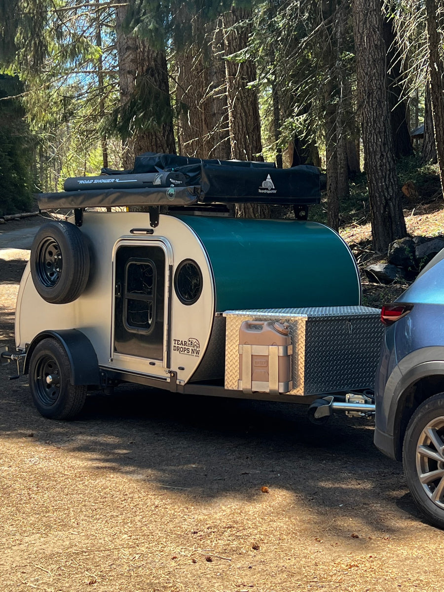 parked in a sunlit forest campsite with a picnic table.|A Teardrops NW teardrop RV rental