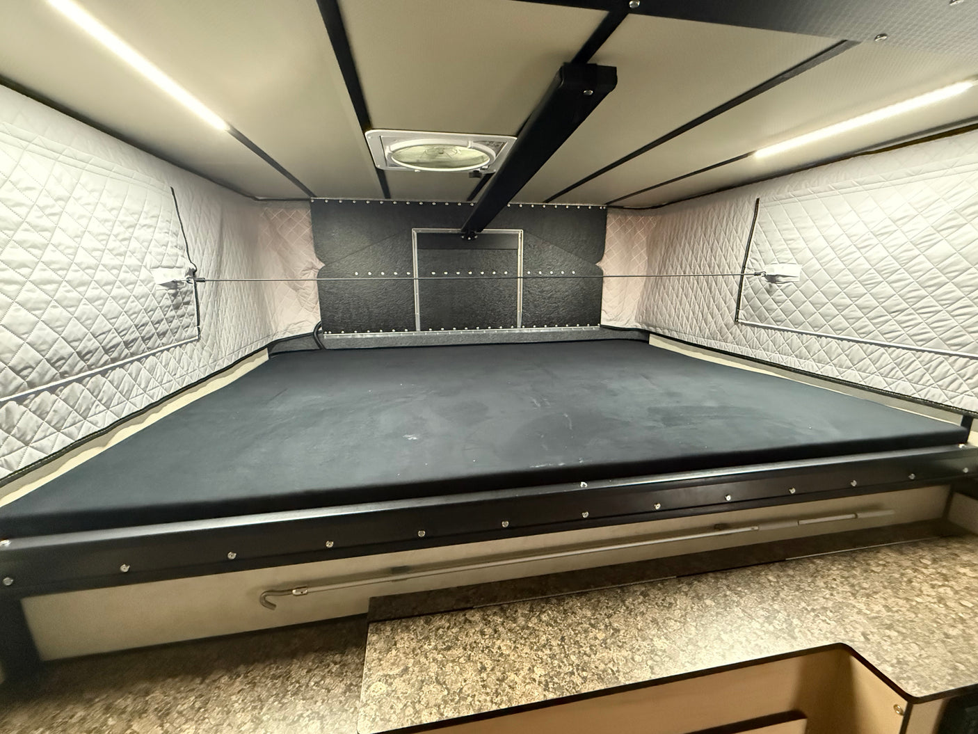 RV rental interior: A raised bed platform, ceiling fan, LED lights, quilted wall insulation, and lower counter space.