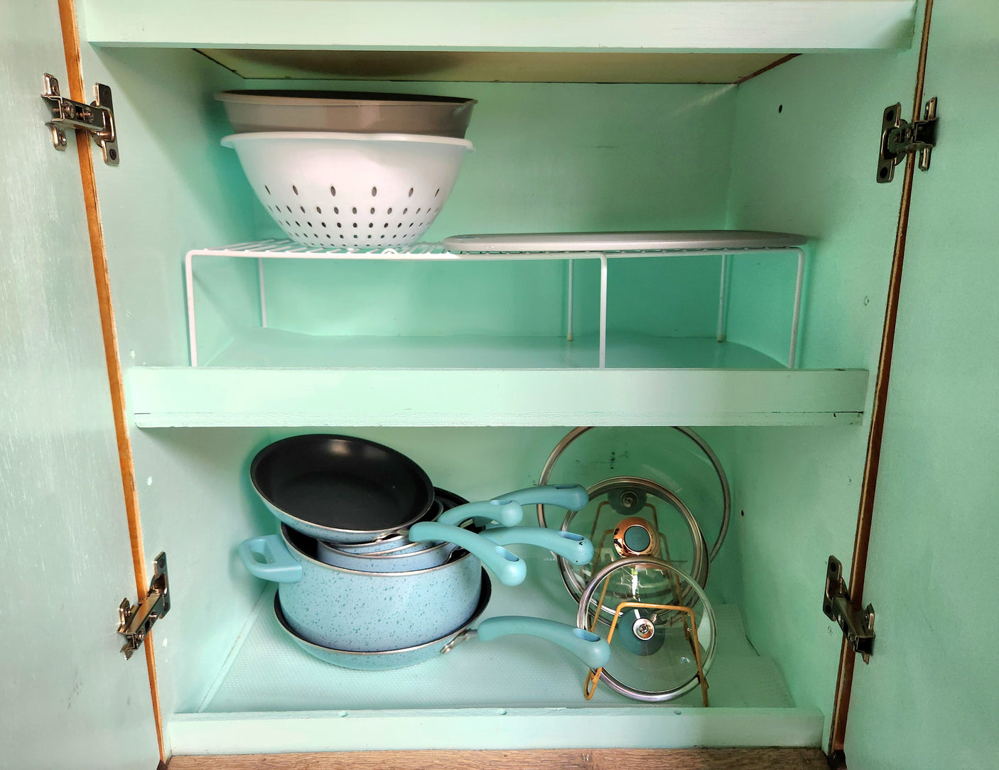 RV rental kitchen cabinet with neatly organized blue pots, pans, lids, & colanders on shelves.