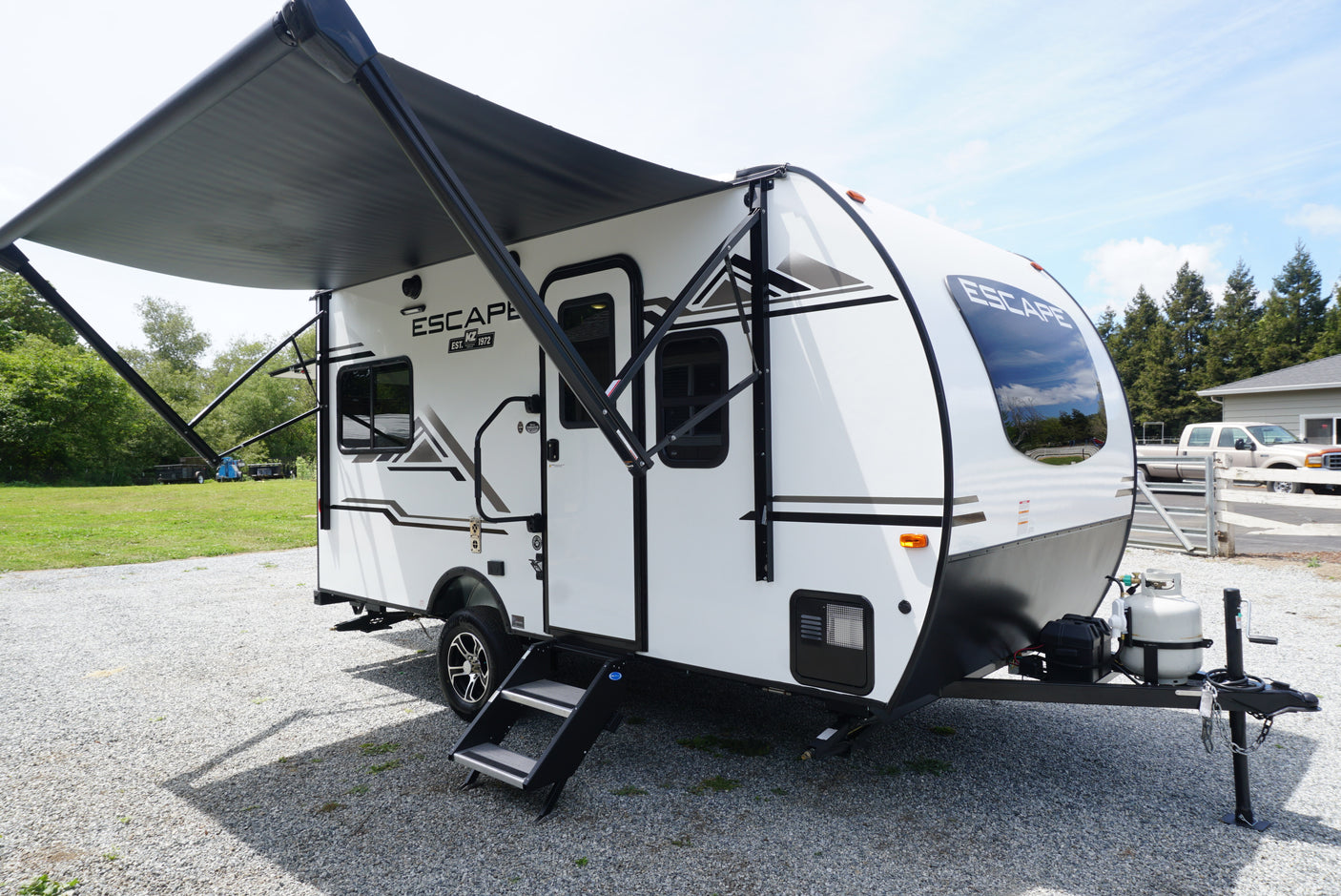 Modern white travel trailer RV with black accents and extended awning on gravel. Ideal for RV rental trips.