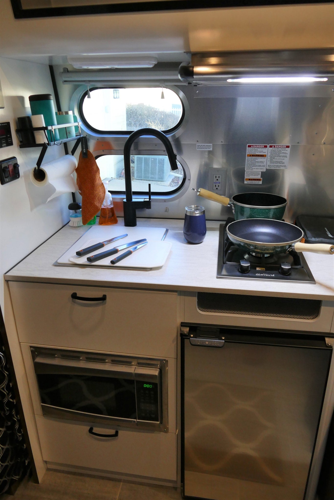 Compact RV kitchen, ideal for an rv rental, featuring a sink, stove, microwave, and refrigerator for cooking on the go.