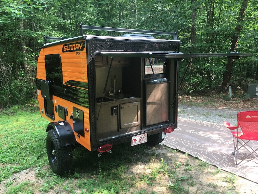 Orange Sunray Sport teardrop RV rental setup at a campsite with its rear outdoor kitchen open.
