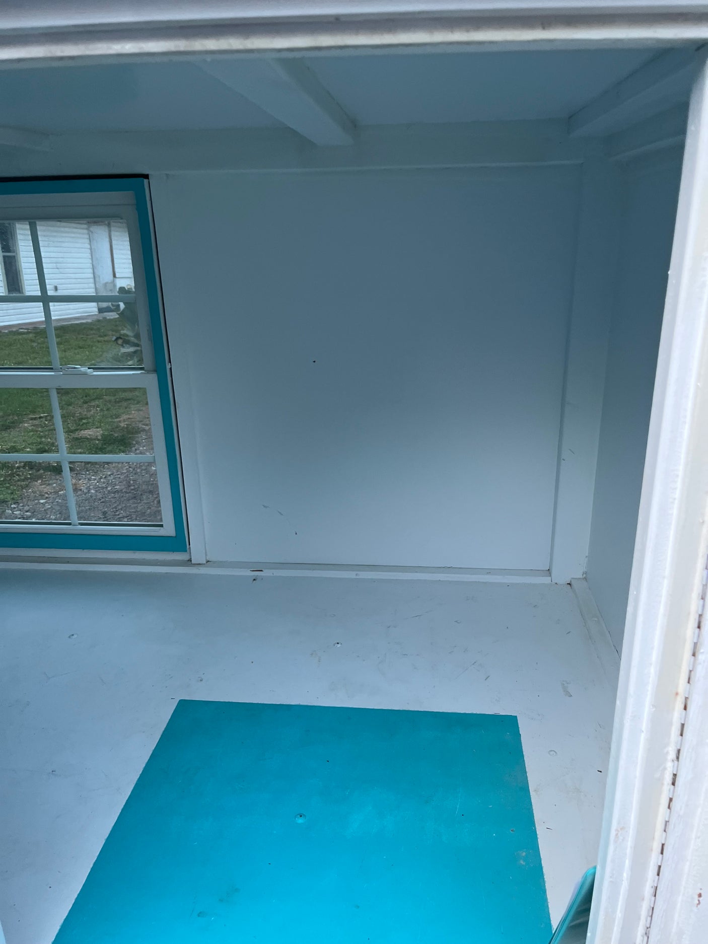 Bright RV rental interior: white walls, ceiling beams, window to outside, and a turquoise floor mat.