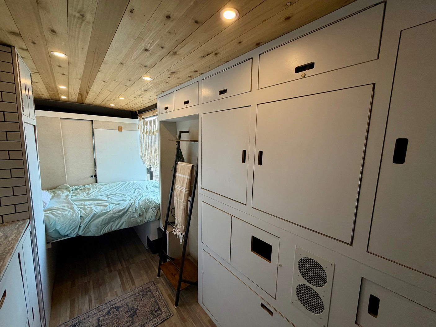RV rental: Cozy camper interior with a bed, wooden ceiling, tiled counter, and integrated storage units.