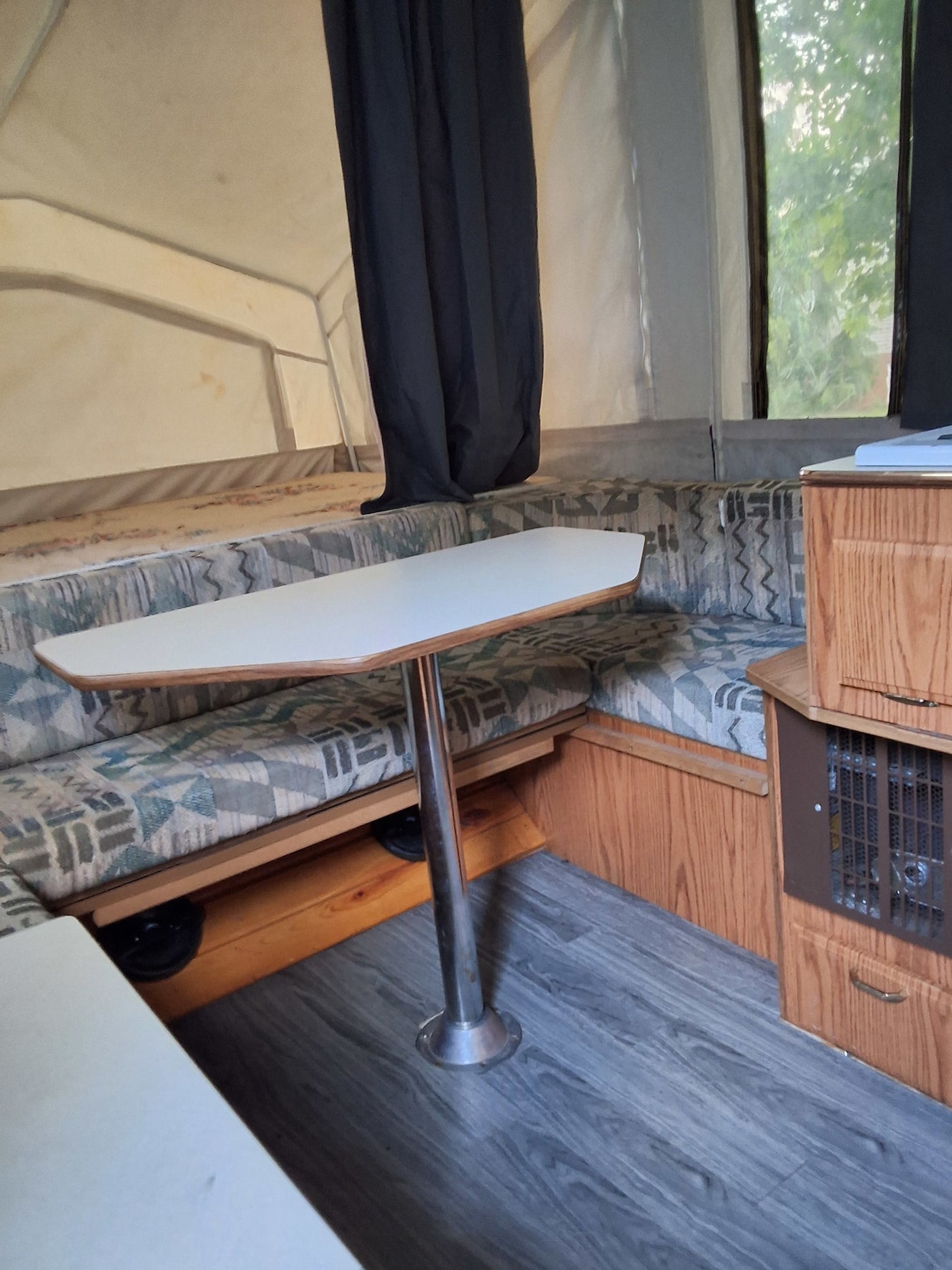 Inside an RV rental, showing a cozy dinette, patterned cushions, wood interior, and window view.