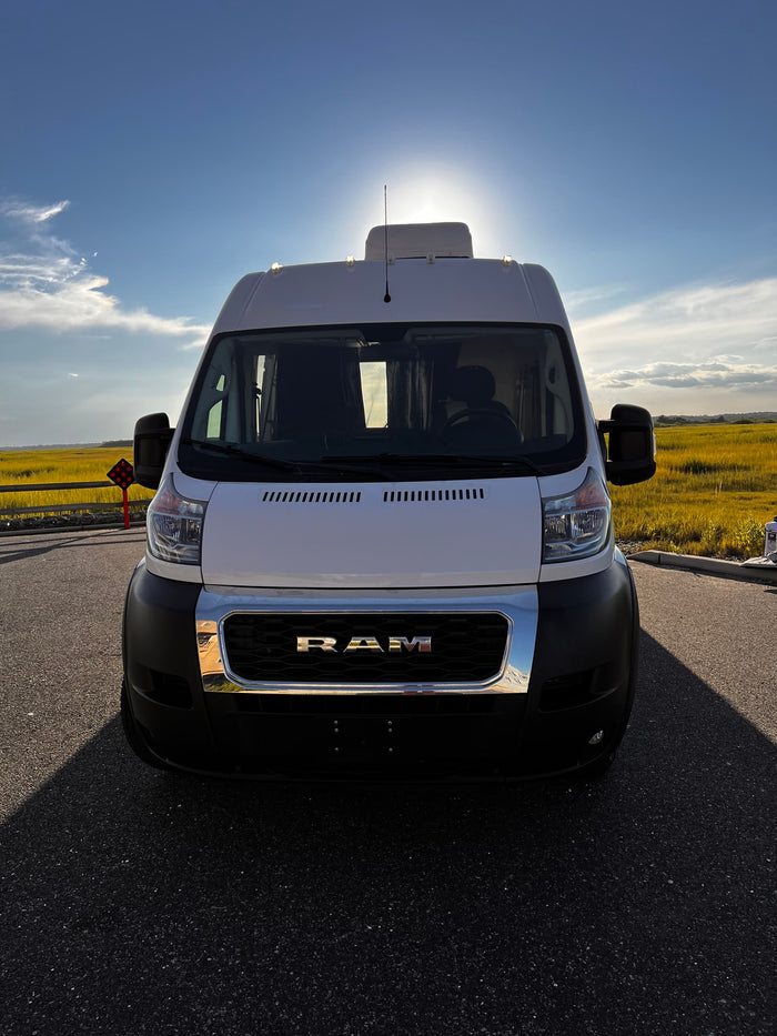 Front view of a white Ram ProMaster van, perfect for an RV rental adventure, parked against a sunny, golden field.