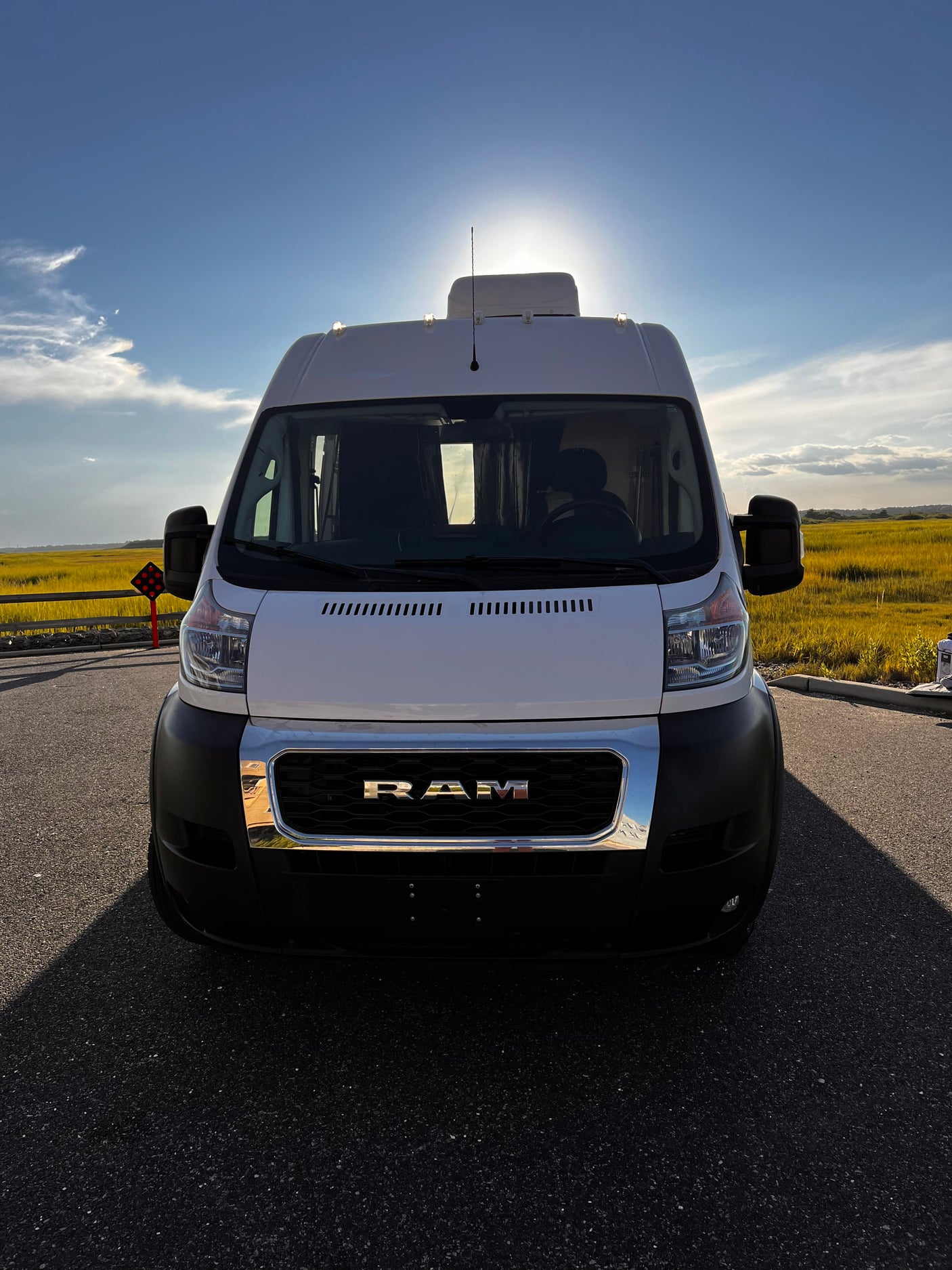 Front view of a white Ram ProMaster van, perfect for an RV rental adventure, parked against a sunny, golden field.