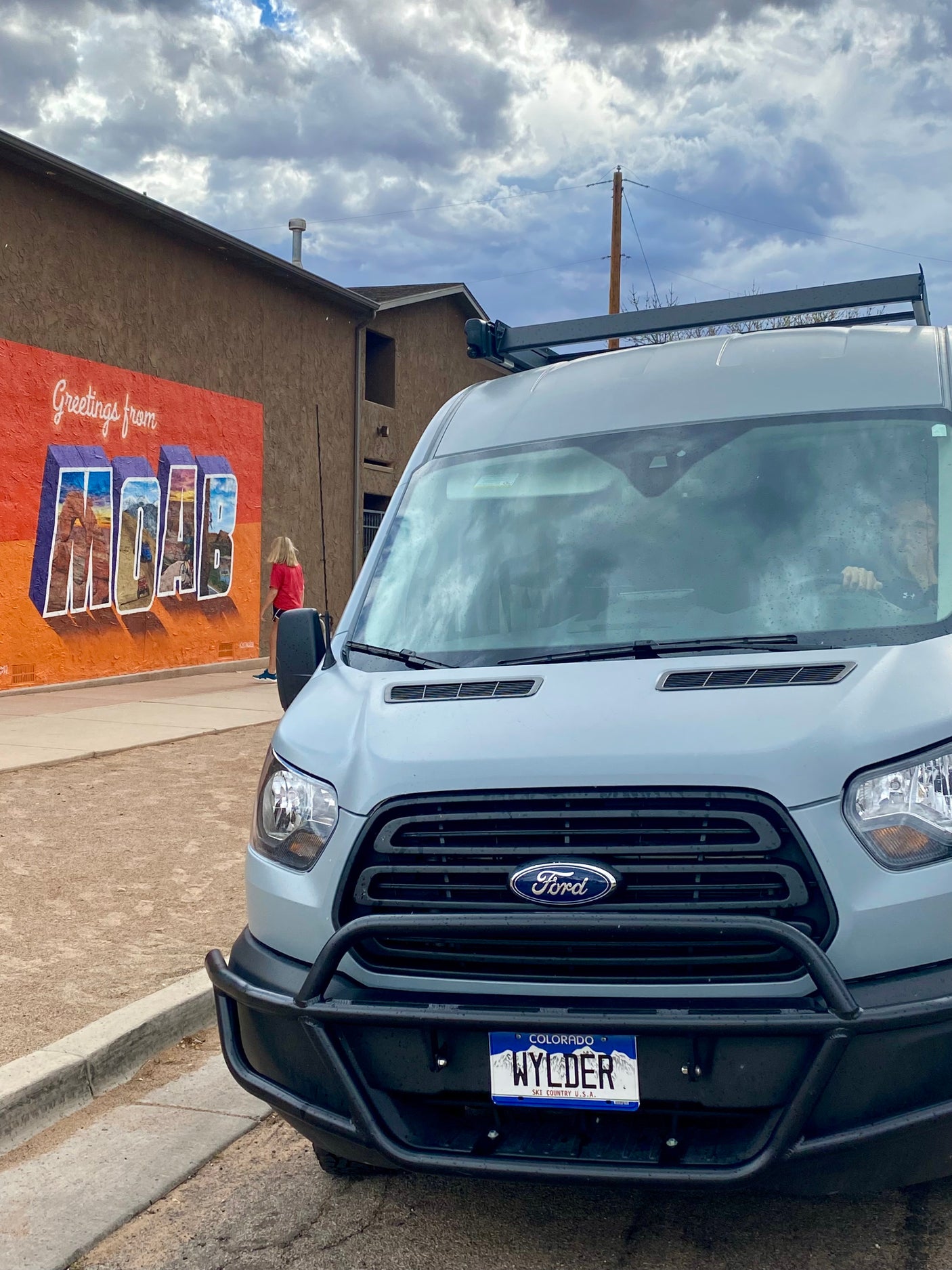 Wylder, a gray Ford Transit RV rental, parked by a "Greetings from Moab" mural. Ready for adventure in Colorado!