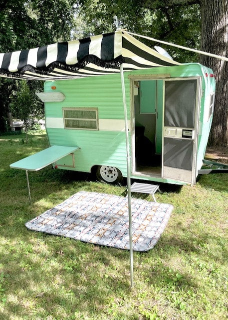 Retro green RV rental with striped awning & side table. Mat on grass for cozy outdoor escape.|Experience the cozy interior of our turquoise RV rental kitchen