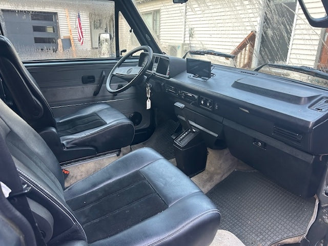RV rental interior: driver's view of a classic camper van with dark seats, steering wheel, and dashboard.