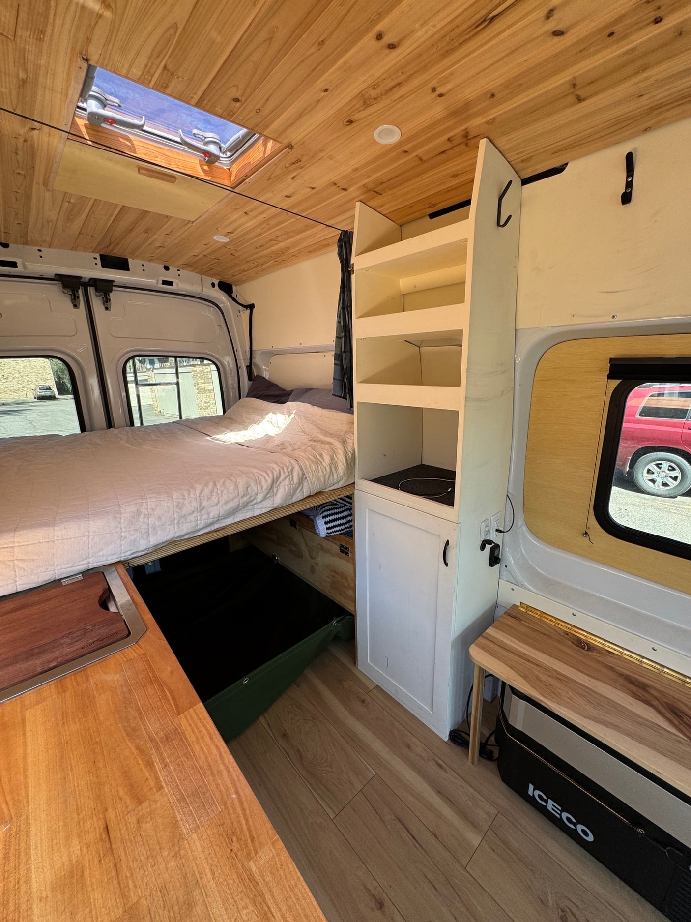 RV rental: Inside a van conversion with a bed, wood-paneled ceiling, compact kitchen counter, and white storage.