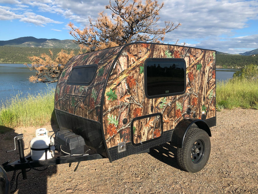 Camouflage teardrop camper RV rental by a lake and mountains. Ideal for off-road outdoor adventures.|Explore the outdoors with this unique camouflage teardrop camper