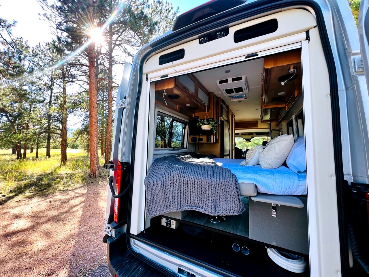 Relaxing RV rental adventure! Cozy campervan interior opens to nature, sun shining through pine trees. — photo 4