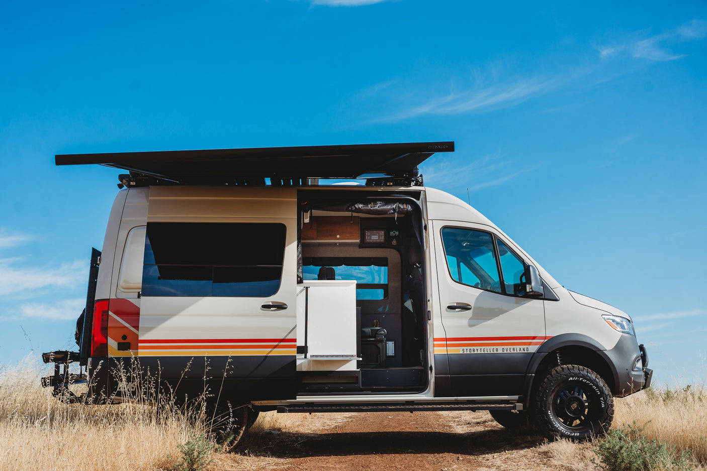 Storyteller Overland MODE van, an adventure-ready RV rental, parked outdoors. Its side door is open, revealing the camper interior.