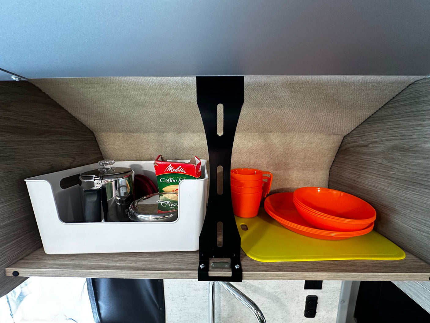 Compact RV rental kitchen storage: coffee essentials, orange dinnerware, & cutting boards neatly stowed on a shelf.