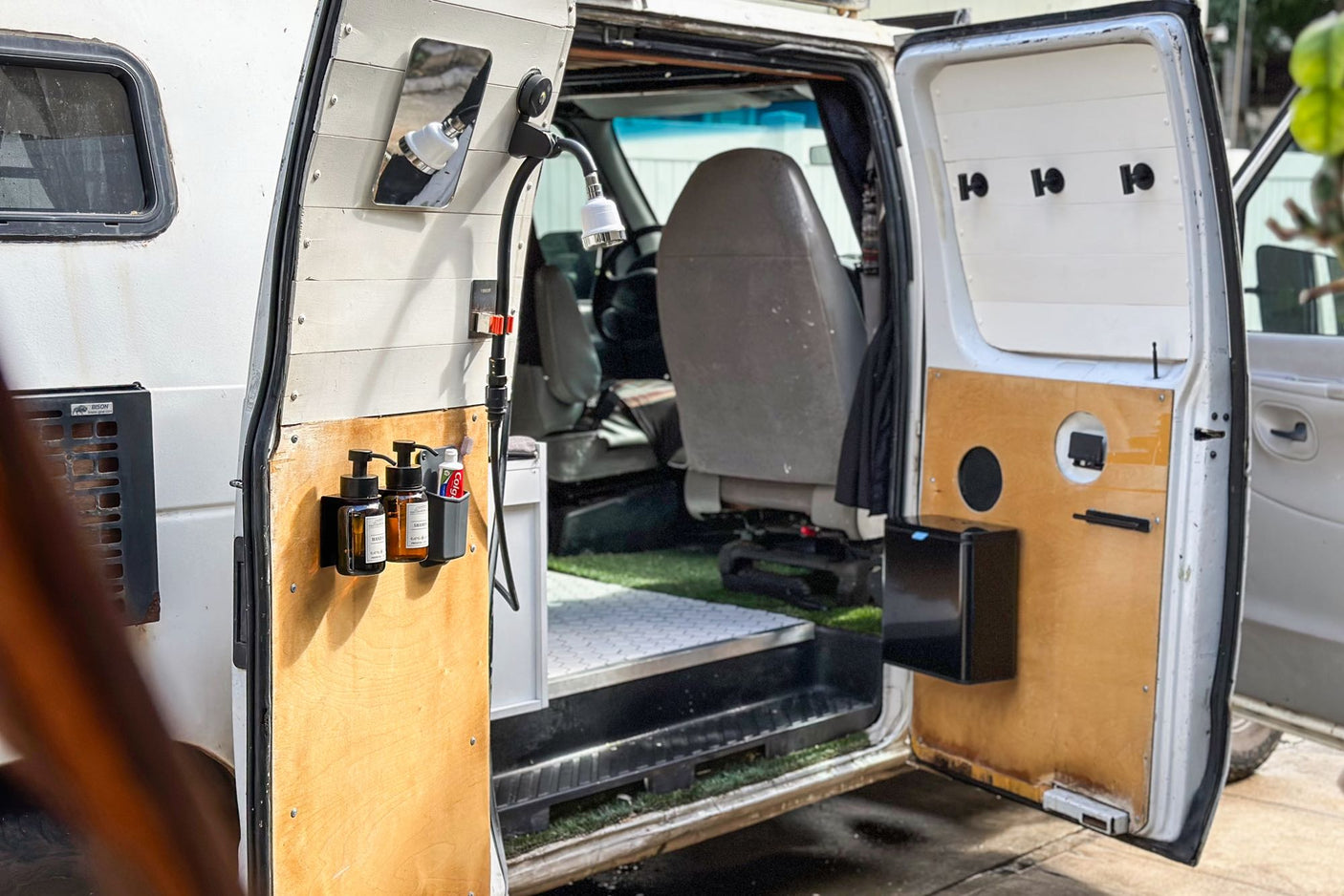 enjoying a game projected on a screen in her custom mobile living space.|This RV rental camper van features a clever outdoor shower with soap and smart storage for road trips.|A woman takes an outdoor shower from her custom camper van