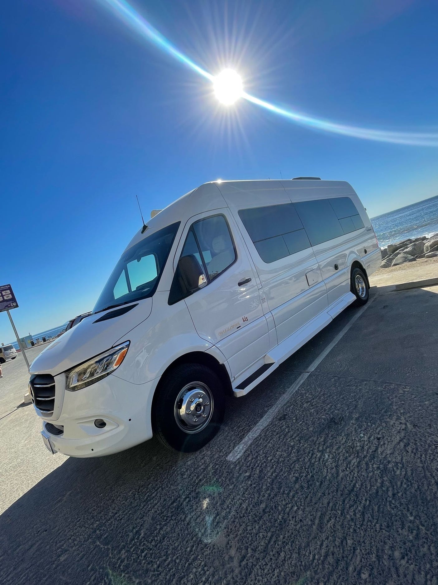A pristine white Roadtrek Galleria camper van, available for rv rental, parked by the ocean on a sunny day.