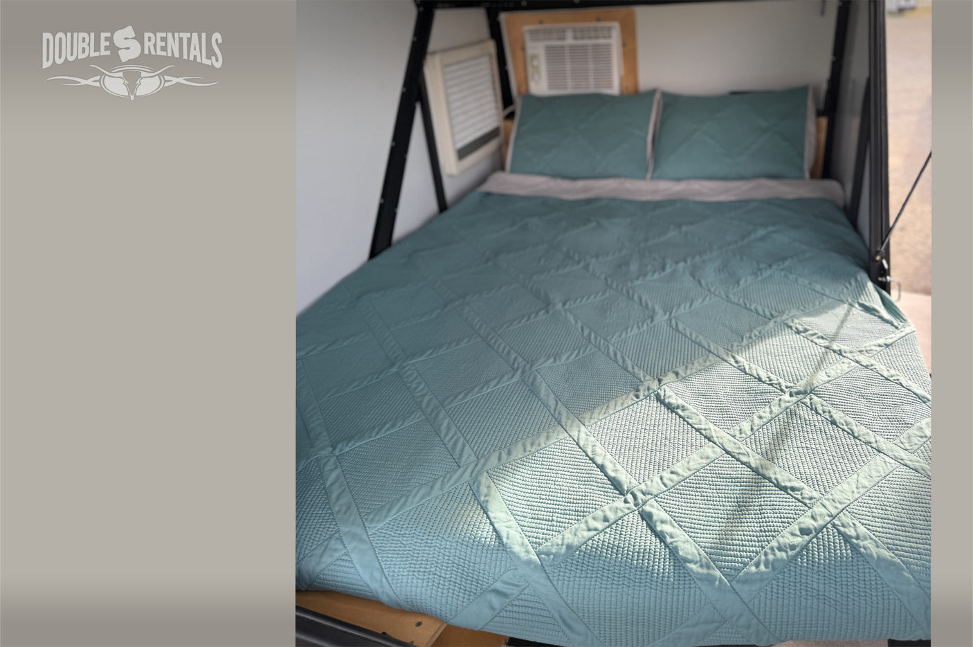 Inside our RV rental: A comfy bed with a quilted teal bedspread, pillows, and AC for your trip.