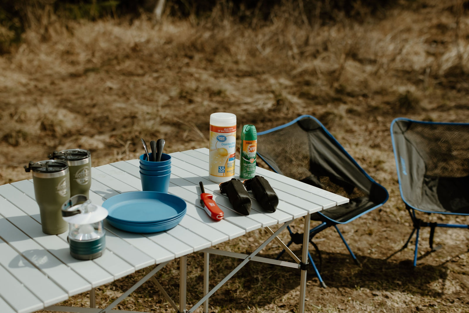 RV rental trip ready! Portable camping table with gear: wipes, repellent, cups, and chairs for outdoor fun.