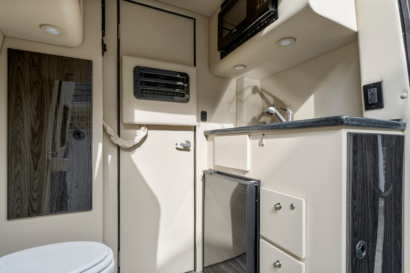 RV rental interior featuring a compact kitchen with microwave, sink, fridge, and a partial view of the bathroom.