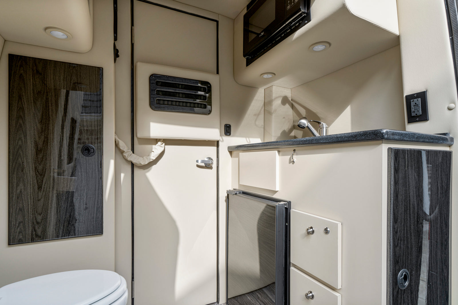 RV rental interior featuring a compact kitchen with microwave, sink, fridge, and a partial view of the bathroom.