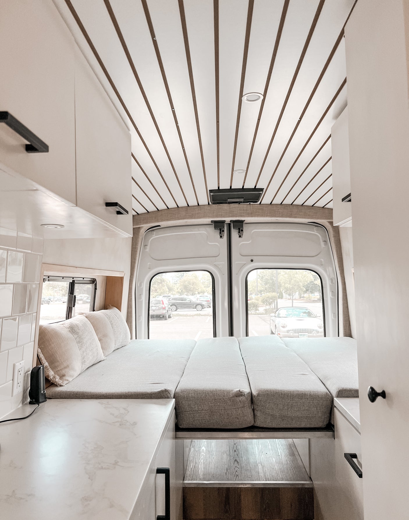 Modern RV rental interior: convertible bed, white and brown slatted ceiling, bright kitchen area.