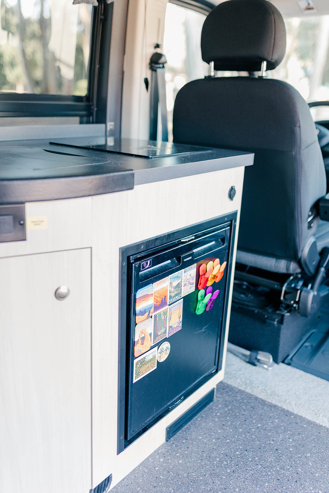 Inside this RV rental, find a compact kitchen with a sleek cooktop and a mini-fridge decorated with travel magnets, ready for adventures.