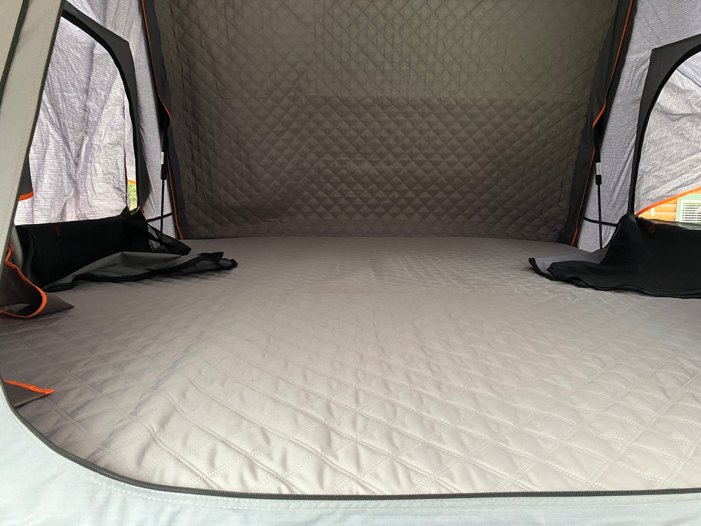 Inside a cozy RV rental: quilted mattress, dark walls, and bright windows offer a comfortable camping experience.