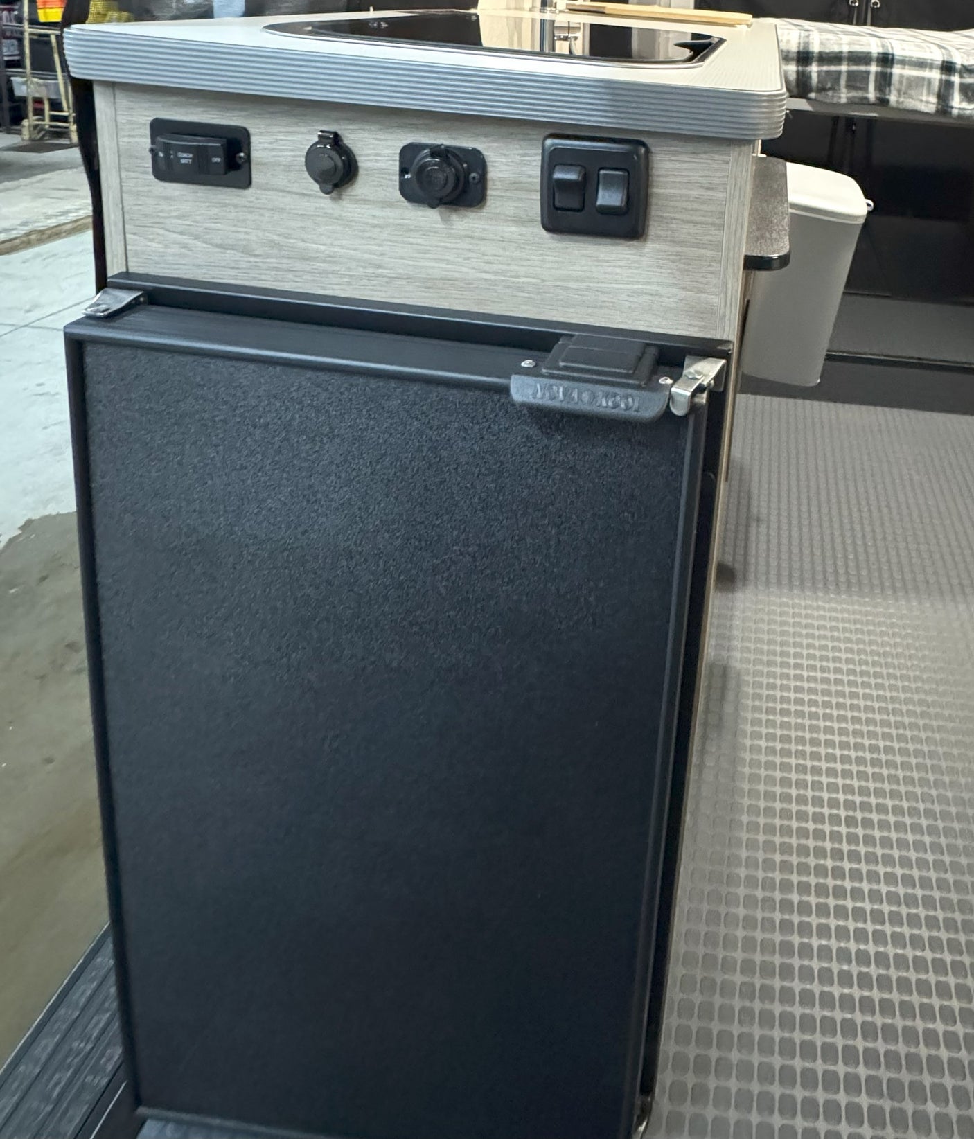 This RV rental utility unit features a compact fridge, 12V outlets, and battery controls below a sink for camper adventures.