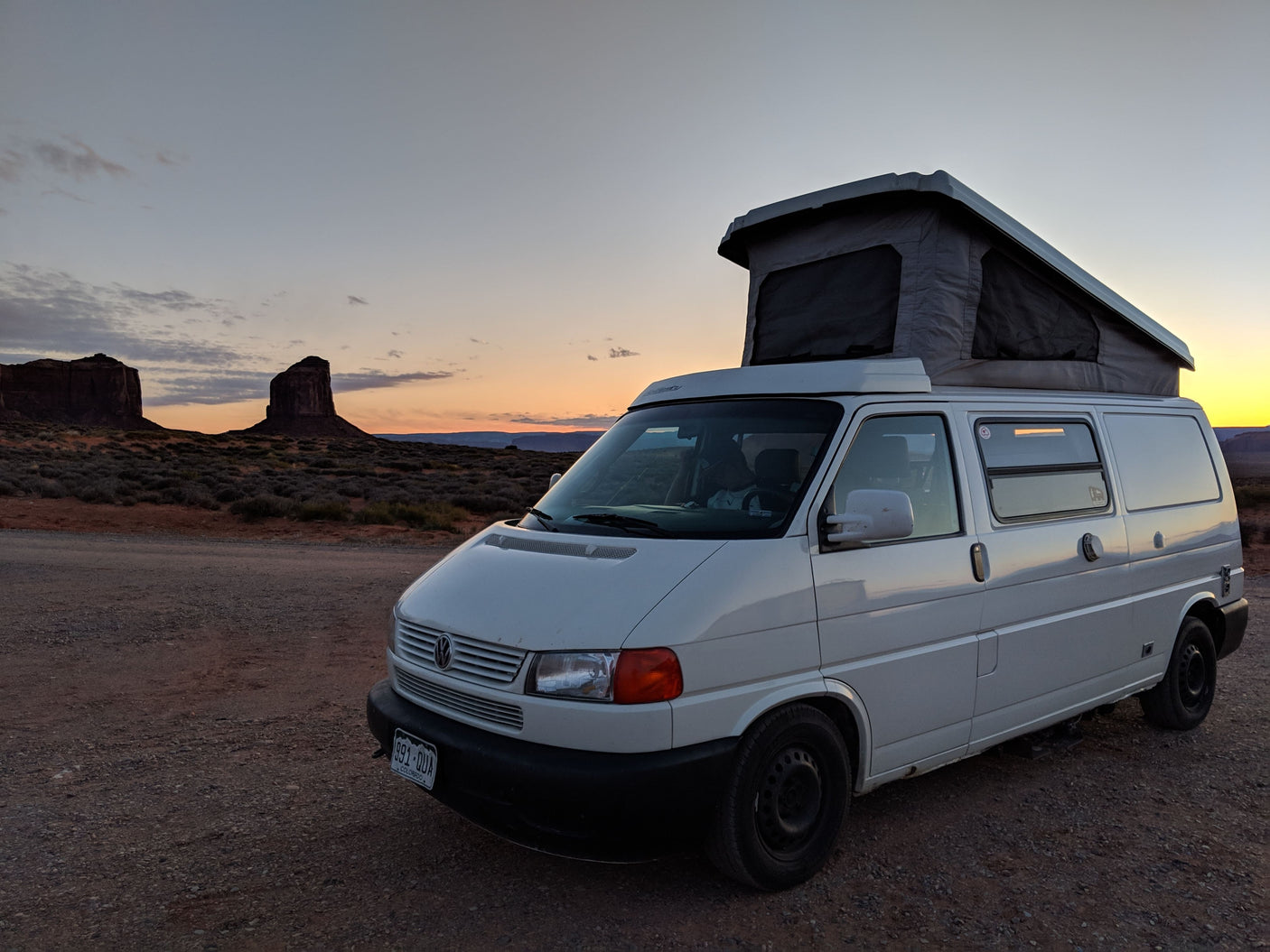 White pop-top camper van for your next RV rental adventure, parked at sunset amidst desert rock formations.