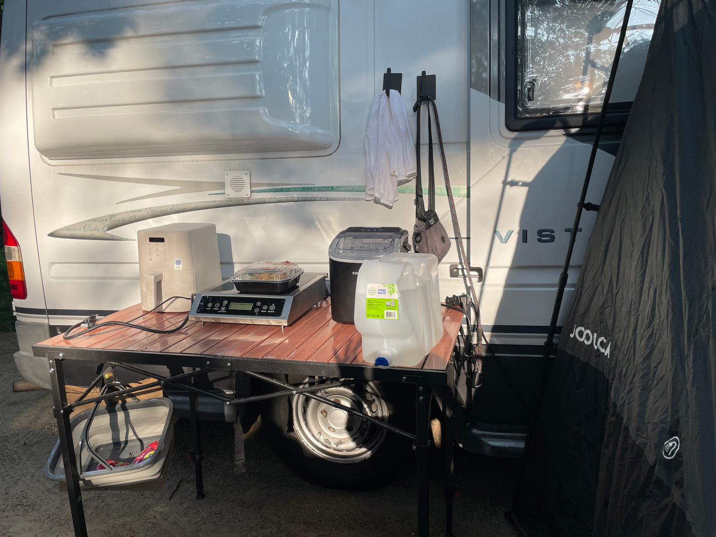 Outdoor cooking setup at an RV rental: air fryer, induction cooktop, ice maker, and water jugs. A Joolca tent is nearby.