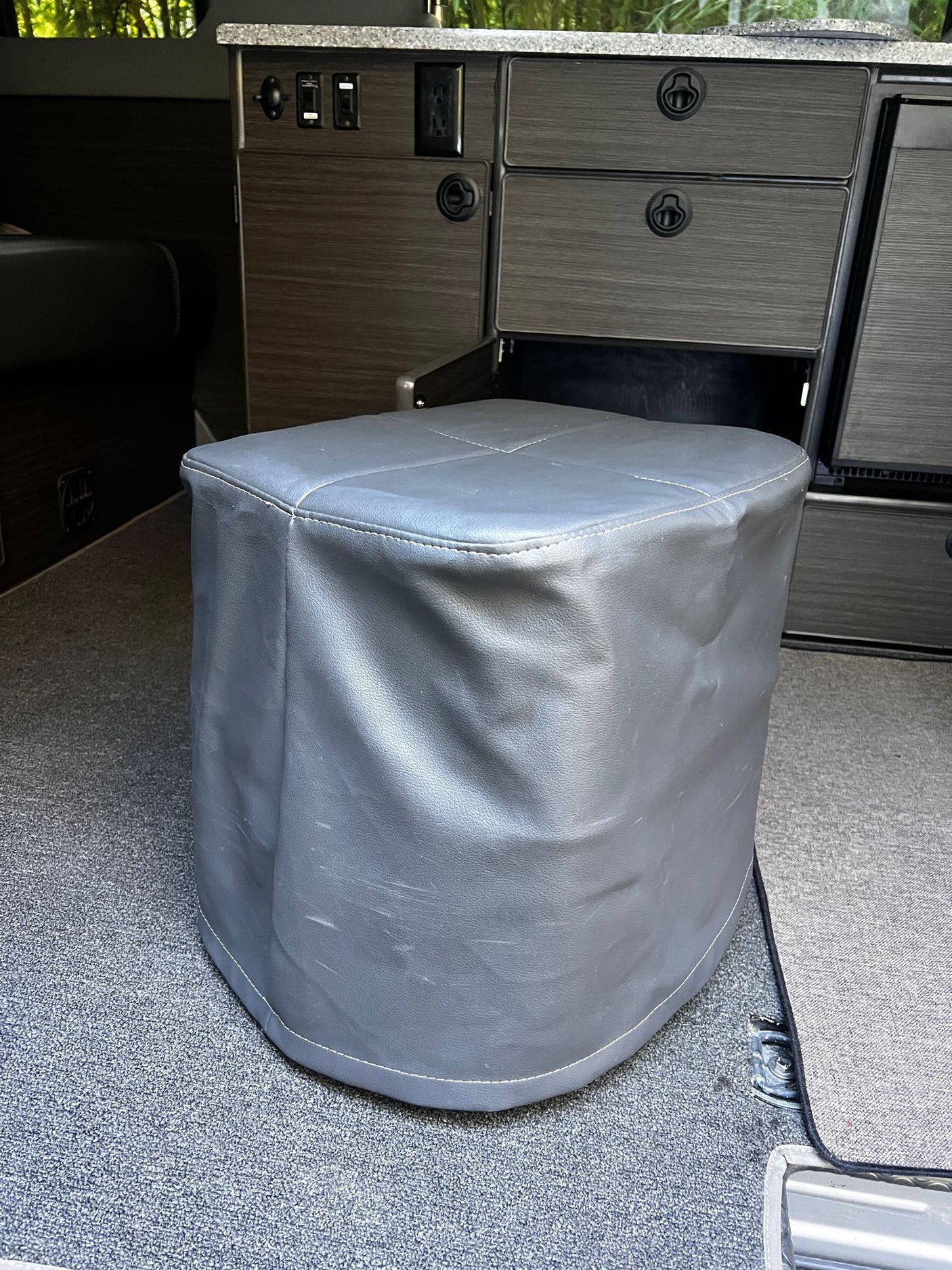 Grey faux leather ottoman in an RV rental, surrounded by custom dark wood cabinetry and carpet.