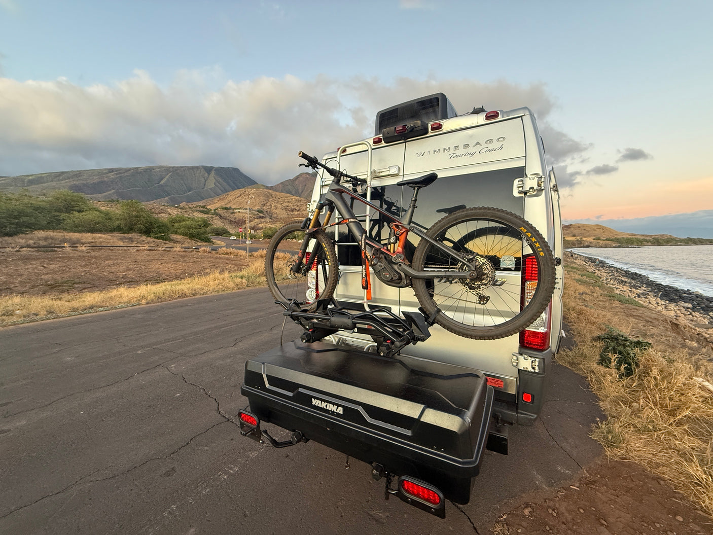 Adventure-ready RV rental, equipped with a mountain bike and cargo box, parked by a scenic coast.