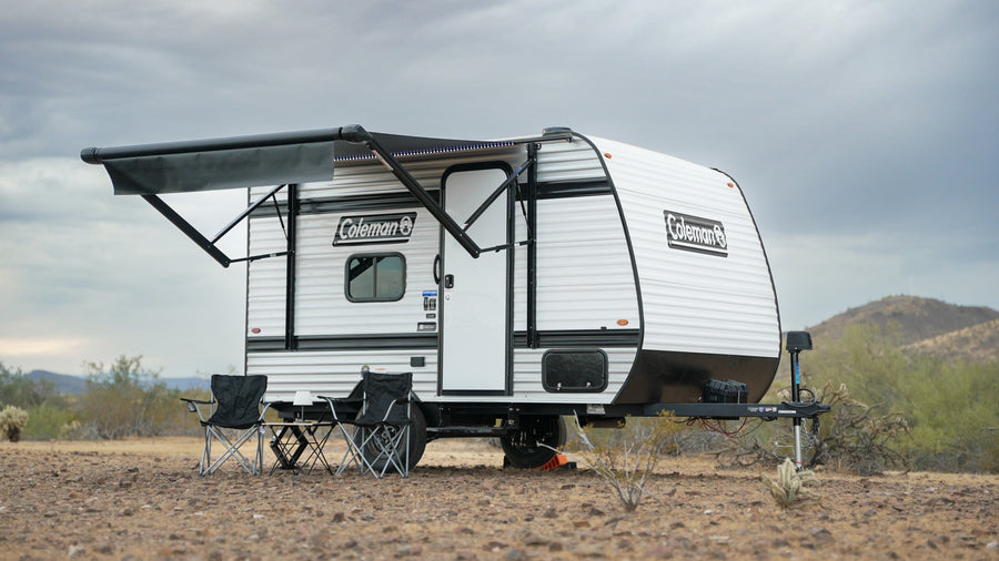 Coleman travel trailer rv rental with an extended awning and chairs set up in a sparse desert landscape under a cloudy sky.