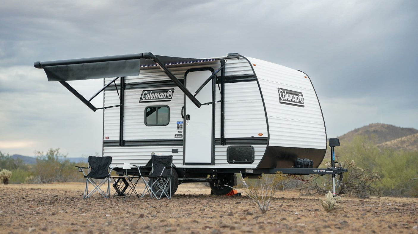 Coleman travel trailer rv rental with an extended awning and chairs set up in a sparse desert landscape under a cloudy sky.