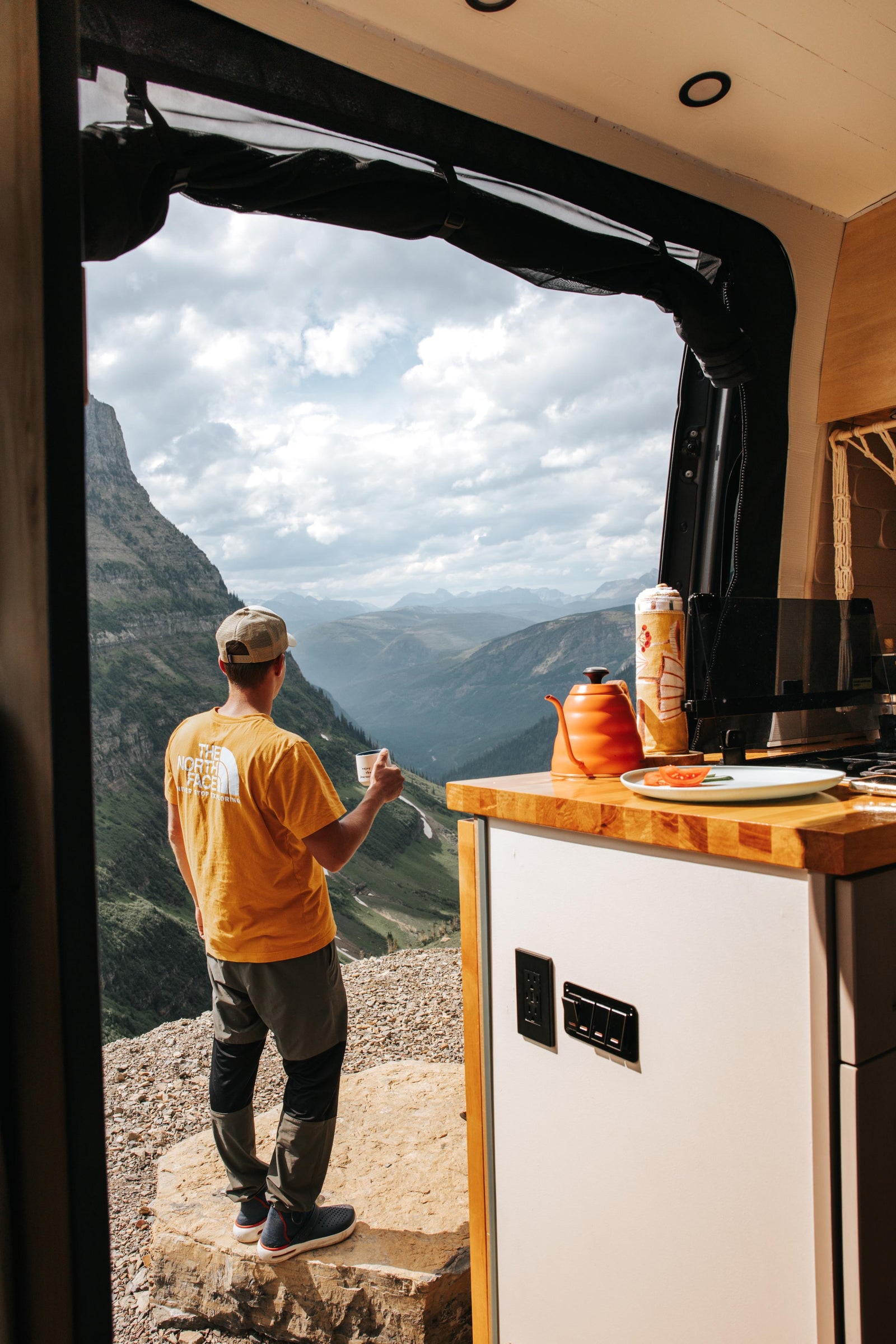cloud-kissed peaks.|RV rental: Man sips coffee from his camper van