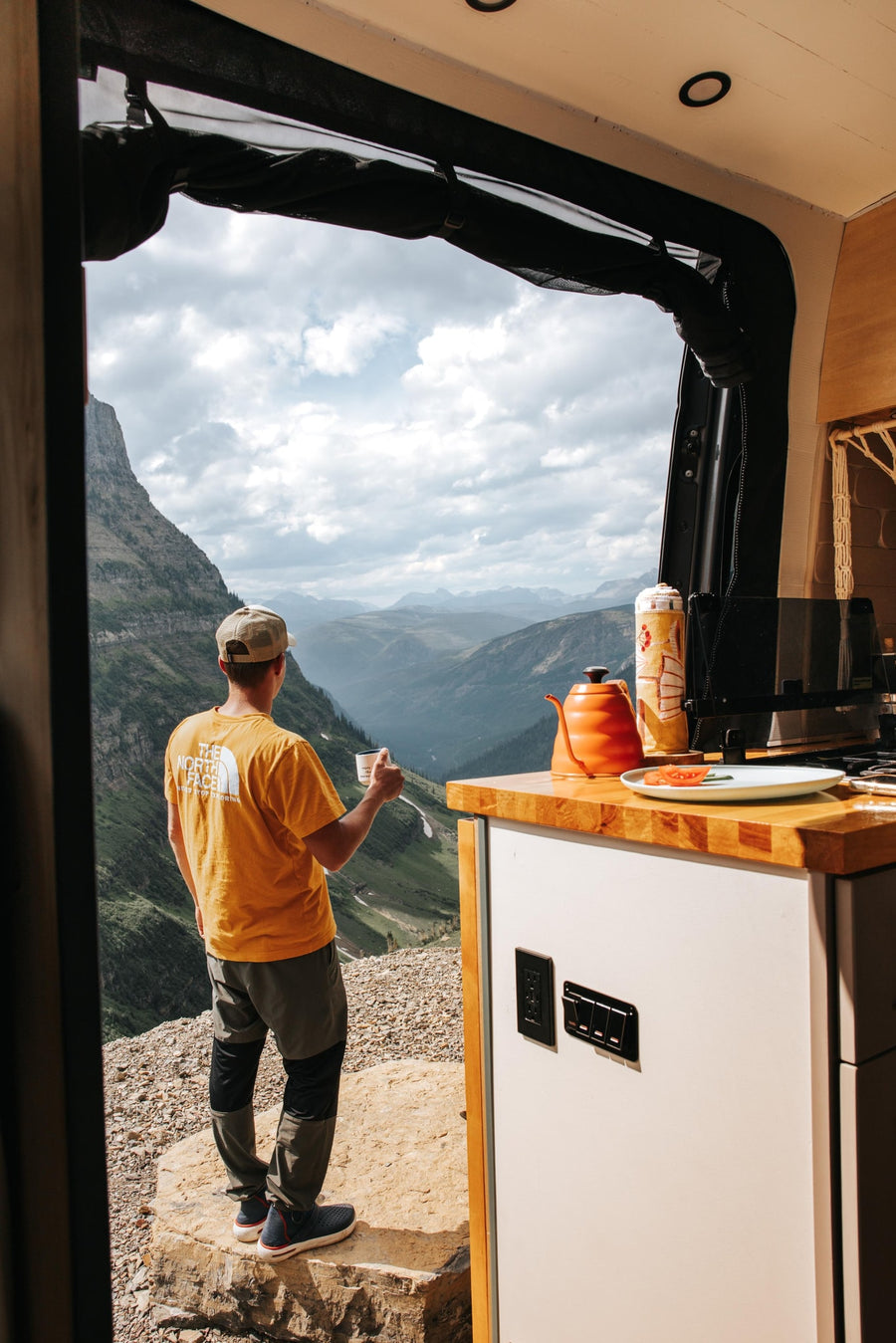 cloud-kissed peaks.|RV rental: Man sips coffee from his camper van