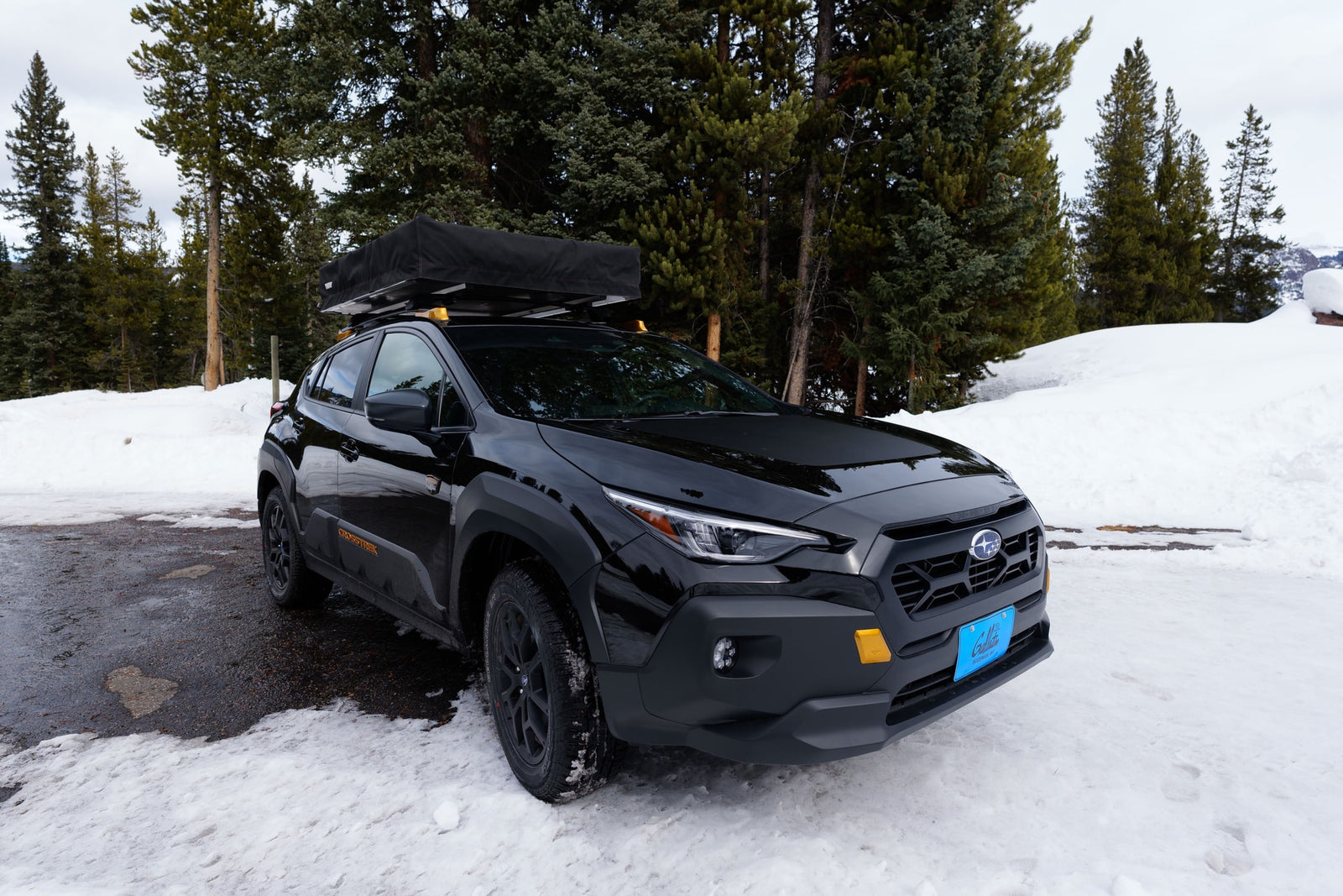 Black Subaru Crosstrek with a rooftop tent for rv rental, parked in a snowy forest. Ideal for winter adventure.