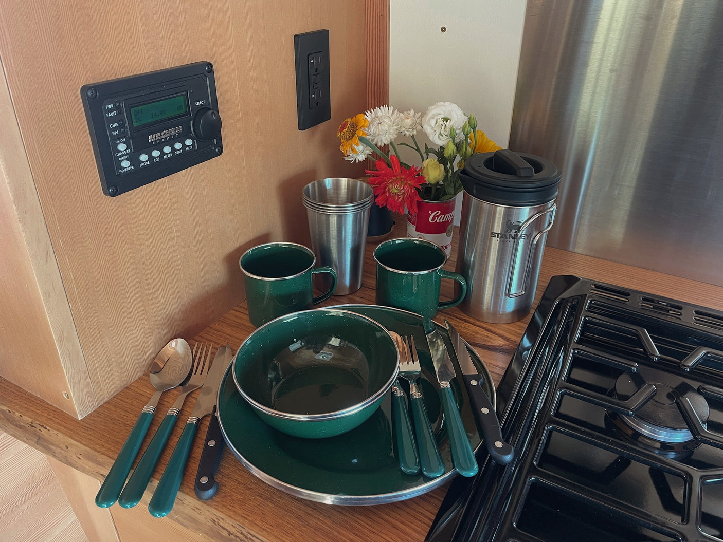 RV rental's equipped kitchen: green enamelware, Stanley mug, stove, and control panel for comfortable camping.