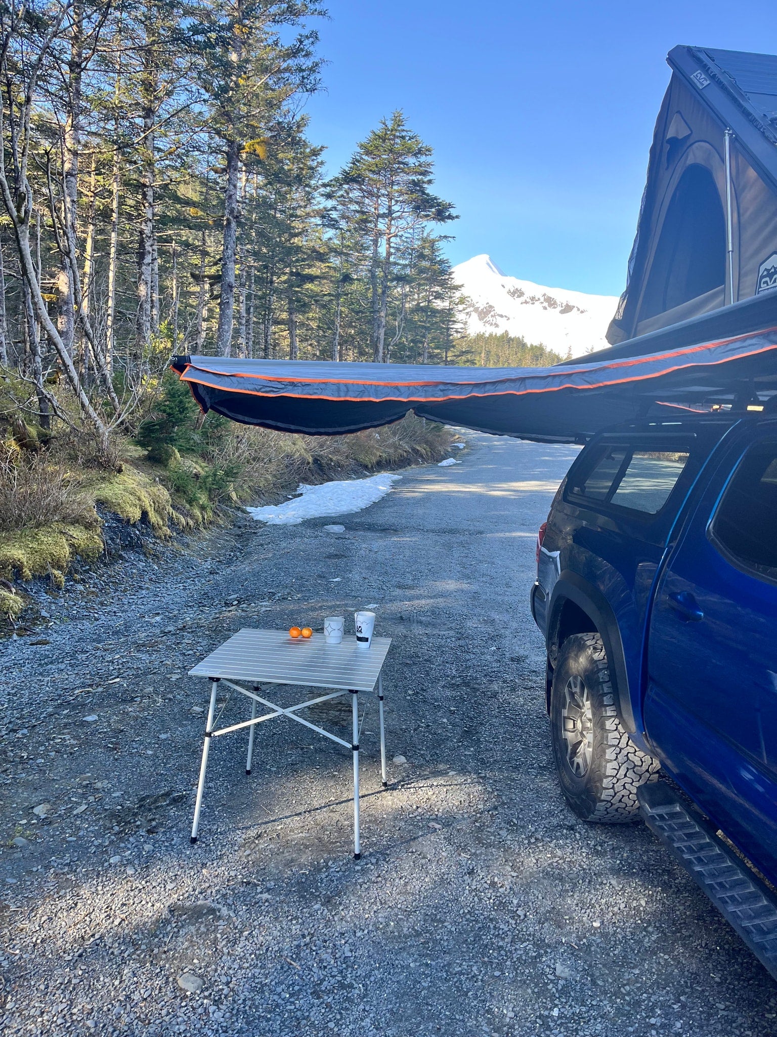 Blue truck with rooftop tent and awning on a mountain road. Ideal for an RV rental outdoor adventure.