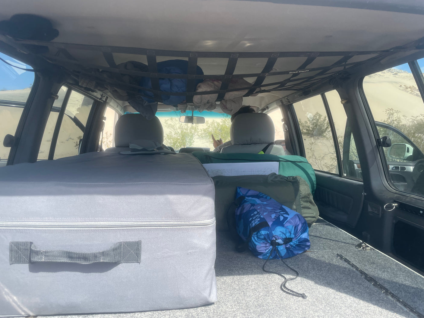 View from the rear of an RV rental, showing a gray sleeping platform, packed bags, and a ceiling storage net with gear for a trip.