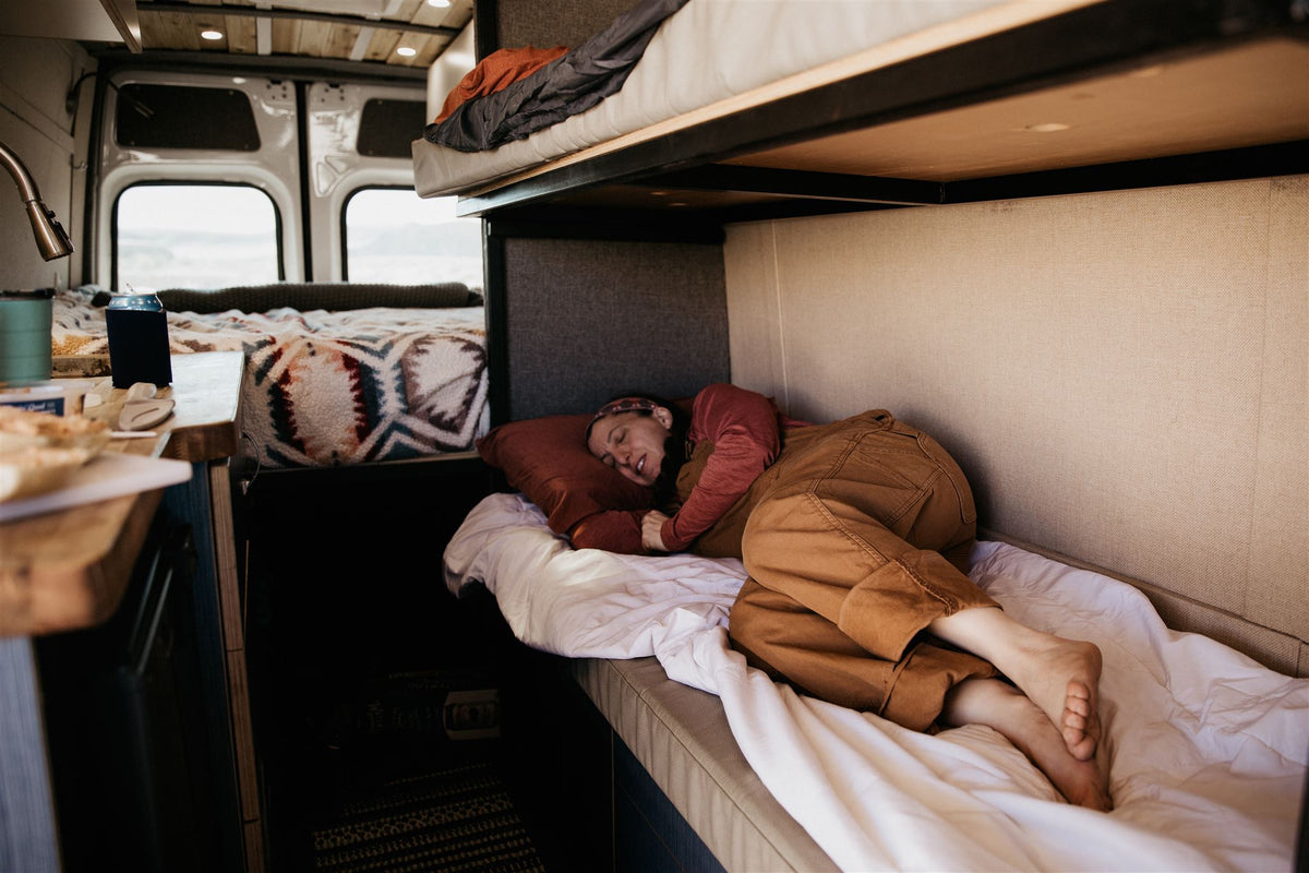 and wooden ceiling. Your adventure awaits!|RV rental interior: A man preparing food in a cozy camper van kitchen with bunk beds & desert views.|Explore a spacious RV rental. This custom camper van features a kitchen — photo 7