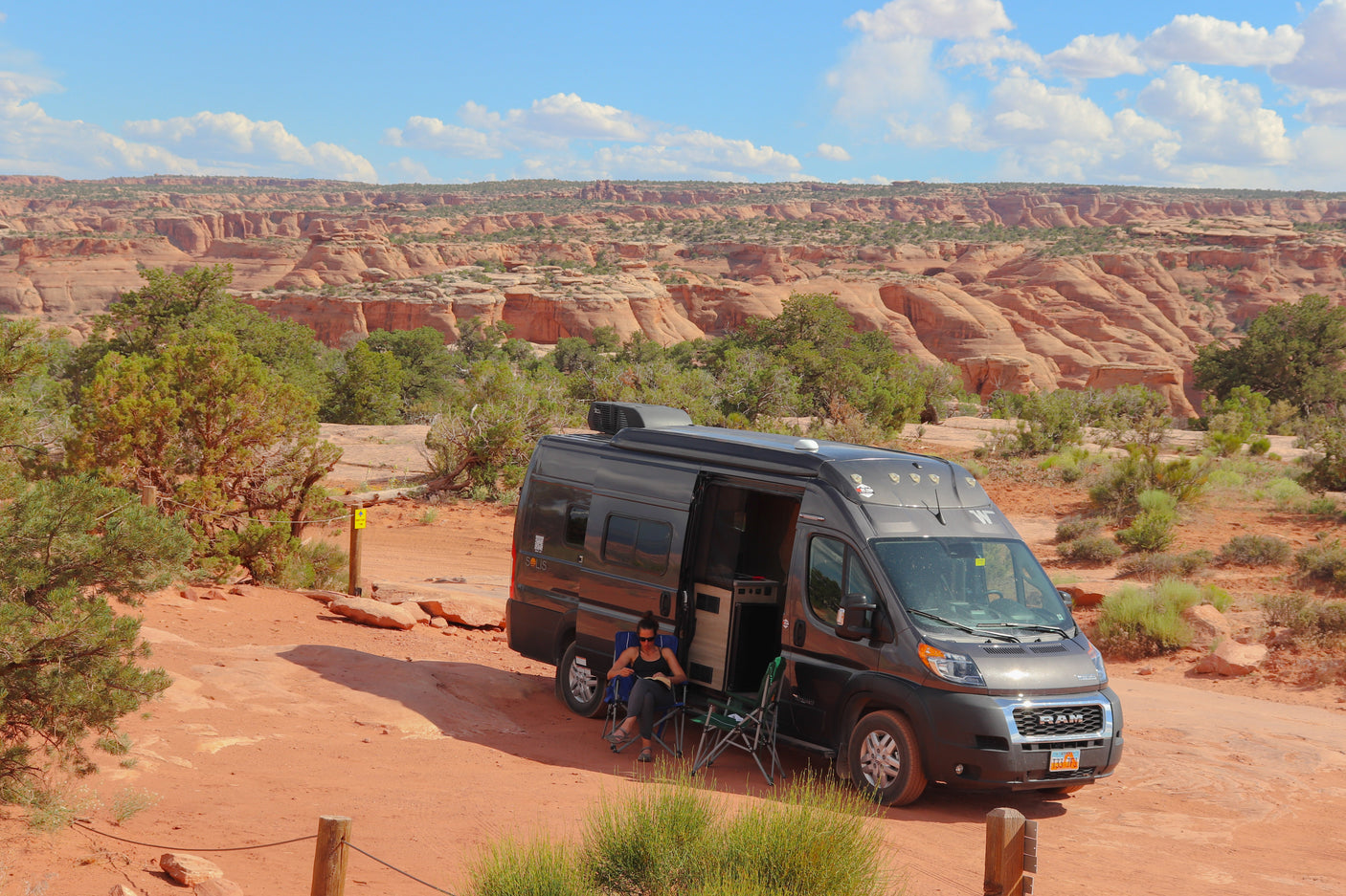 A person reads in an RV rental camper van parked at a scenic red rock canyon campsite, offering stunning desert views.