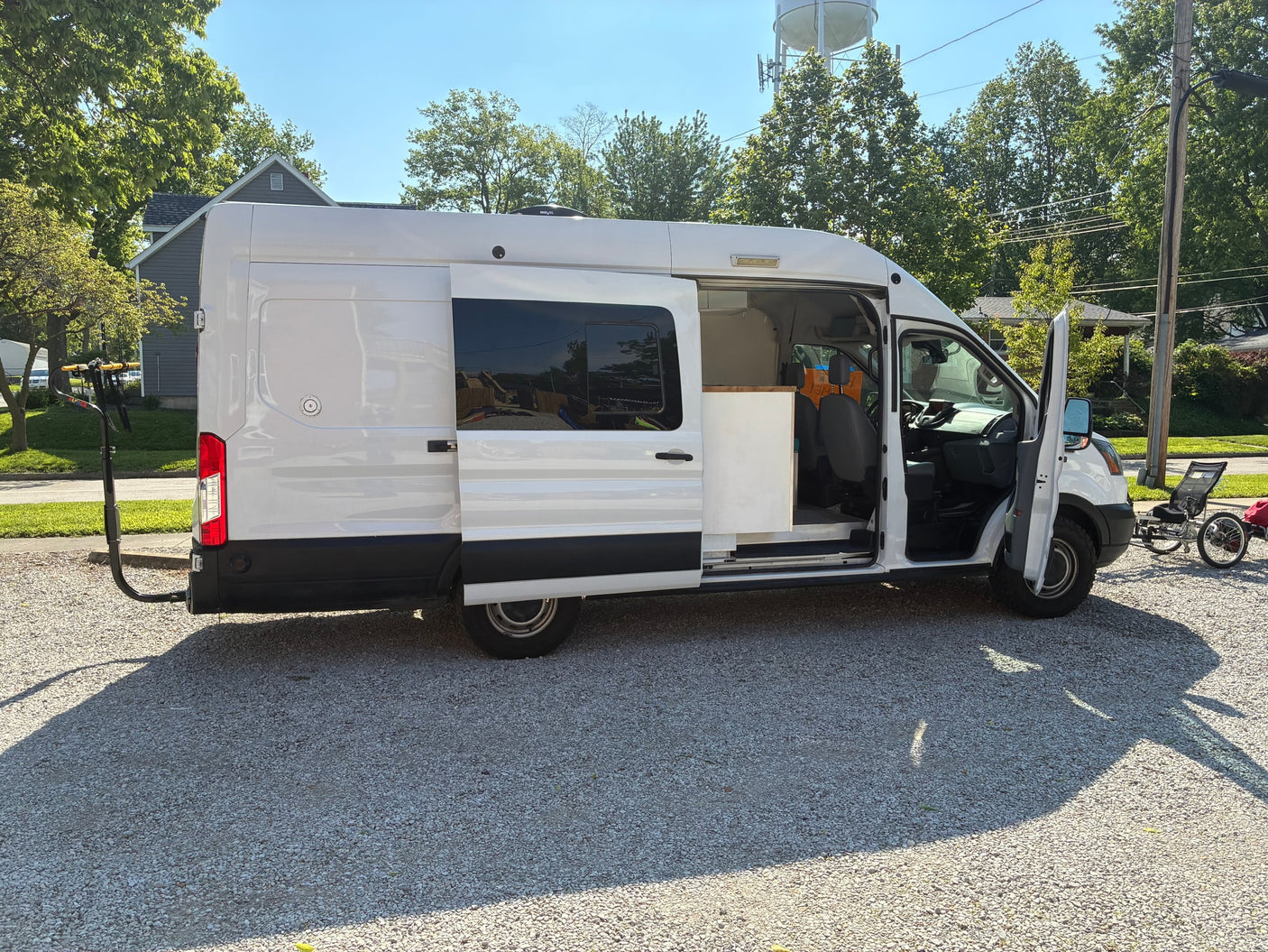 White camper van RV rental with open doors, showing interior, bike rack, and attached recumbent trike.