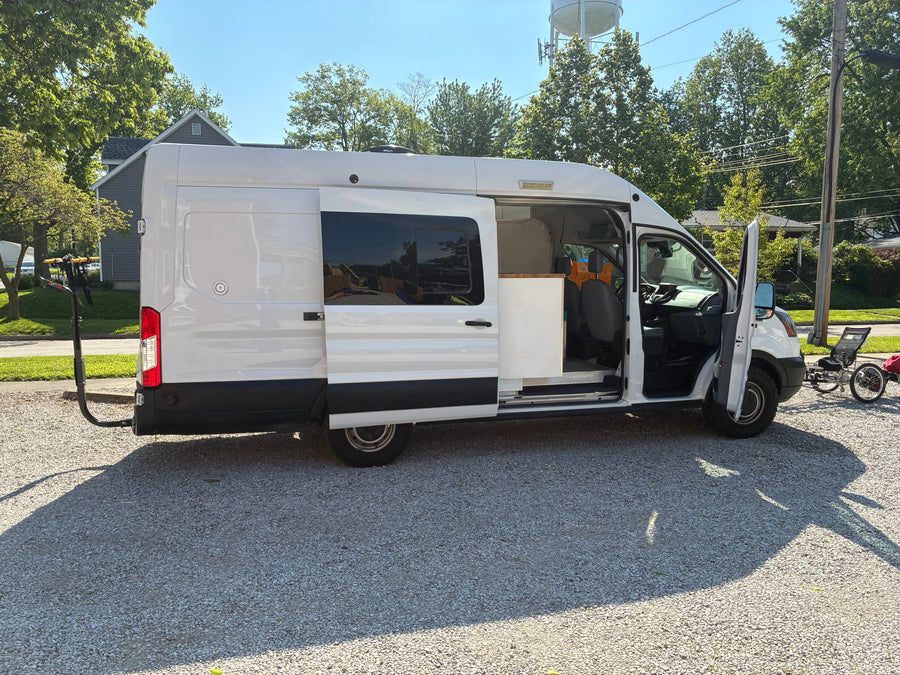 White camper van RV rental with open doors, showing interior, bike rack, and attached recumbent trike.